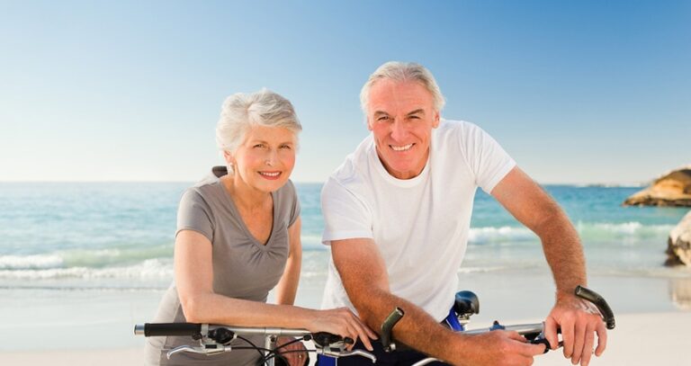 Older Man And Woman On Bikes At The Beach