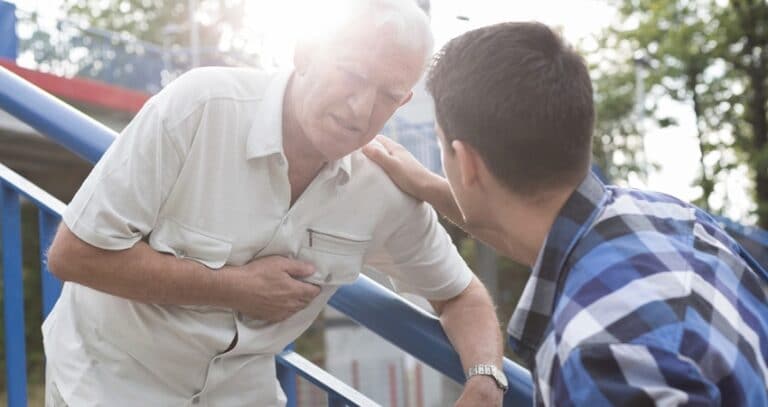 Older Man On Stairs With Heart Distress And Young Man Concerned