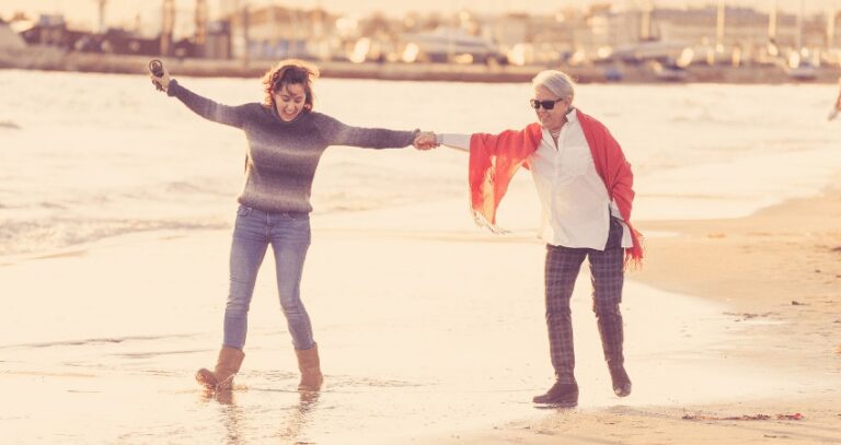 Older Woman And Adult Daughter Enjoying The Beach On A Chilly Day