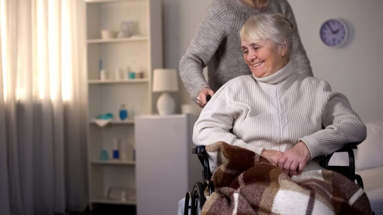 Smiling Woman In A Wheelchair With Her Aide In Her Bedroom