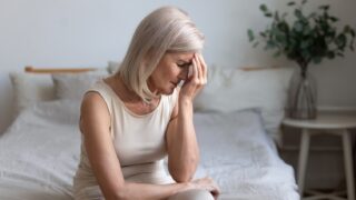 Worried Woman Sitting On Bed Holding Forehead